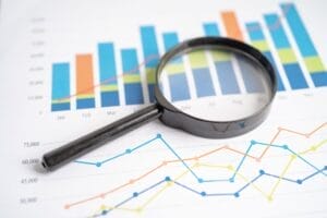 A magnifying glass hovers over paper with bar and line graphs, showcasing statistical data and highlighting keyword tracking for enhanced SEO analysis.