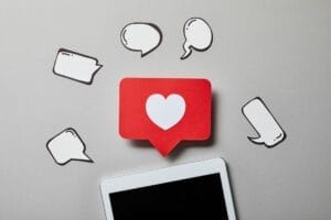 A red speech bubble with a white heart icon and several blank speech bubbles surround a tablet with a blank screen on a gray background, perfectly illustrating the connectivity and engagement central to effective social media marketing.