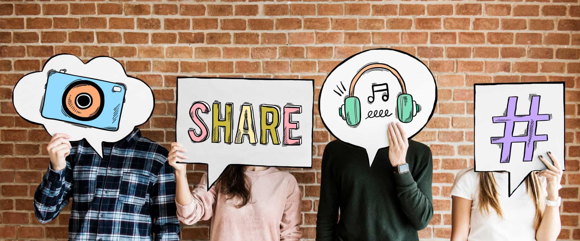 Four people, holding speech bubble signs in front of their faces, display drawings of a camera, the word "SHARE", headphones, and a hashtag symbol against a brick wall background—perfectly capturing the essence of social media marketing.